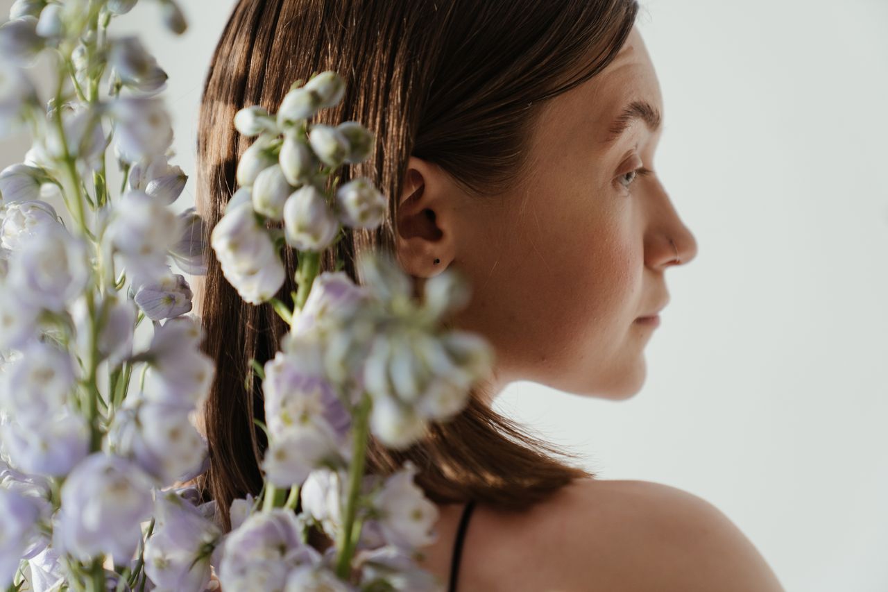 Home A calm portrait of a woman surrounded by delicate delphinium flowers in soft light.